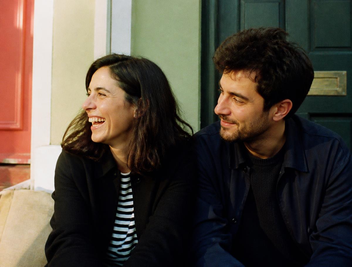 Ana y Roberto, sentados en los escalones de un portal una tarde de primavera; ella ríe mirando fuera de cuadro y él la observa